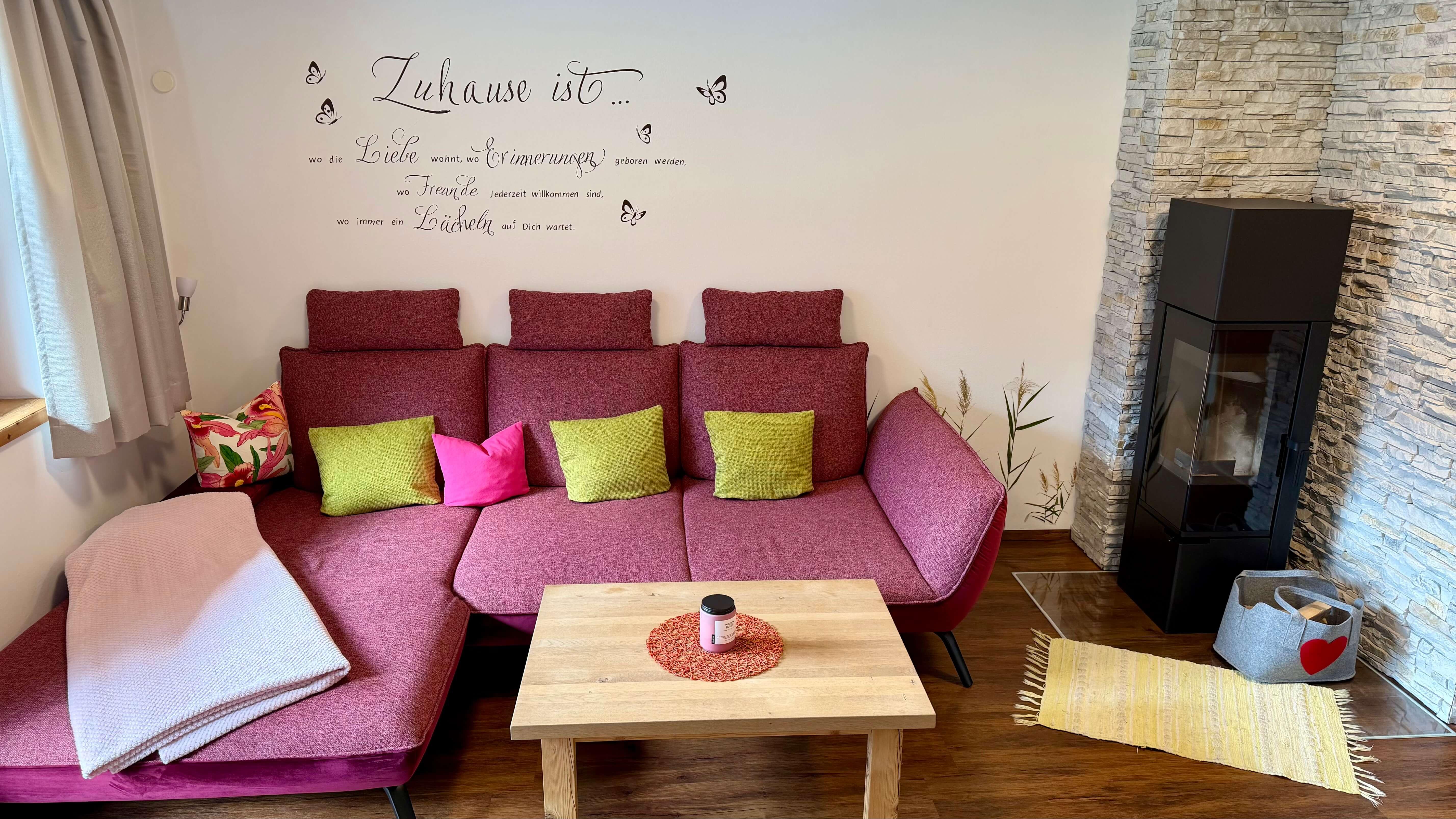 Cozy living room with red sofa, colorful cushions, wall decor, fireplace, and natural light.