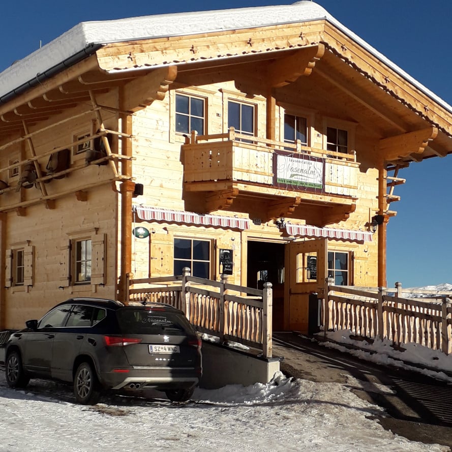 The picture shows the Nasenalm snack bar in winter with a black car and blue sky.