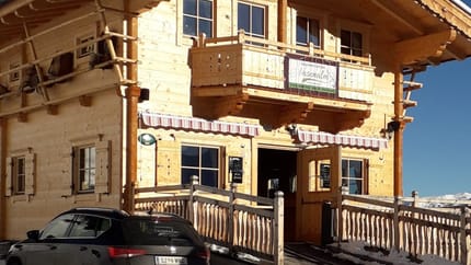 The picture shows the Nasenalm snack bar in winter with a black car and blue sky.