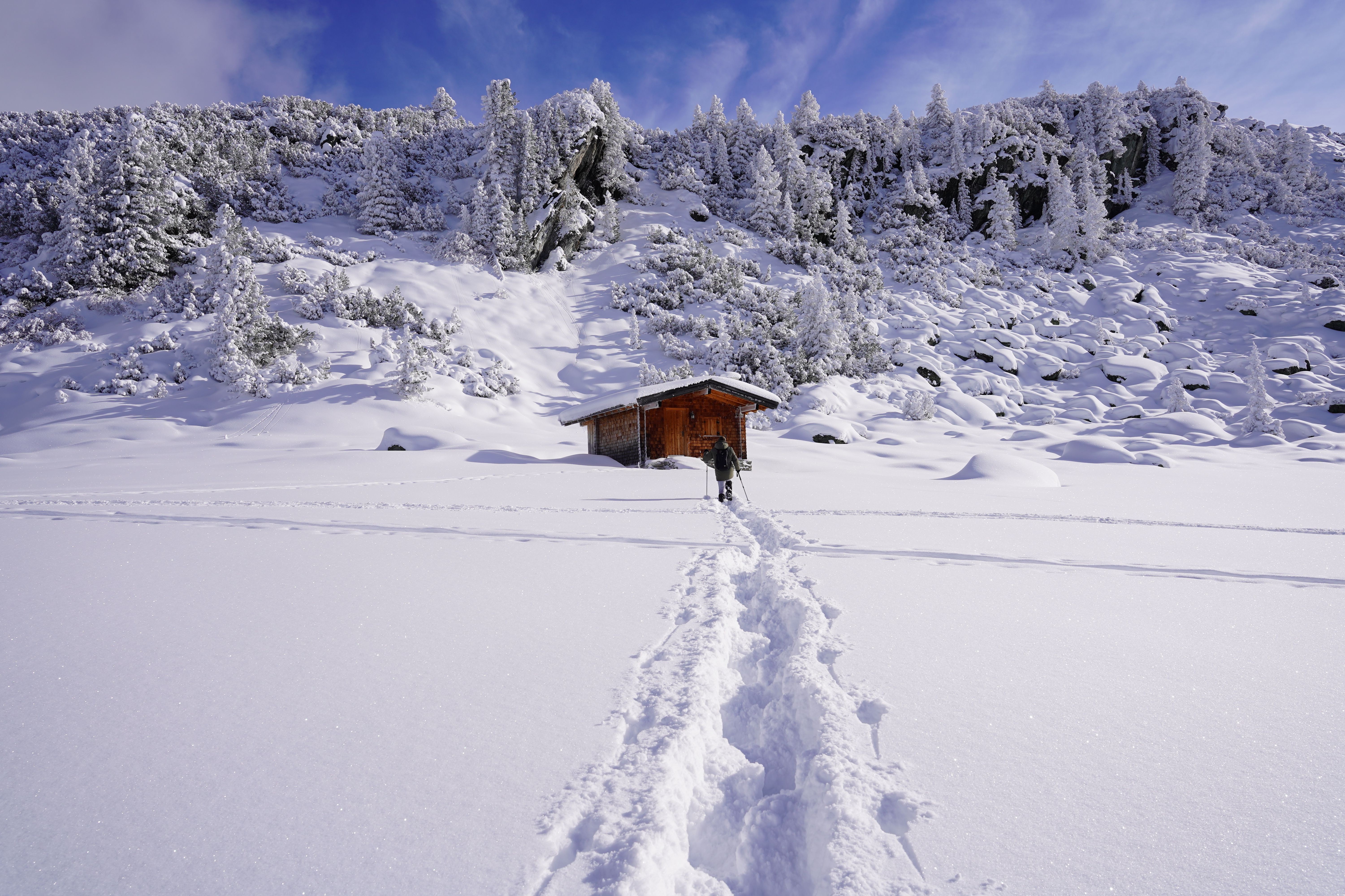 Auf dem Bild ist eine Holzhütte in einer Schneelandschaft zu sehen. Im Hintergrund sind Bäume mit Schnee bedeckt.