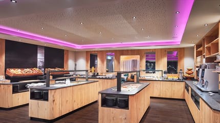 A buffet area in a modern restaurant with wooden cabinets, warm lighting, and various food and drink options.