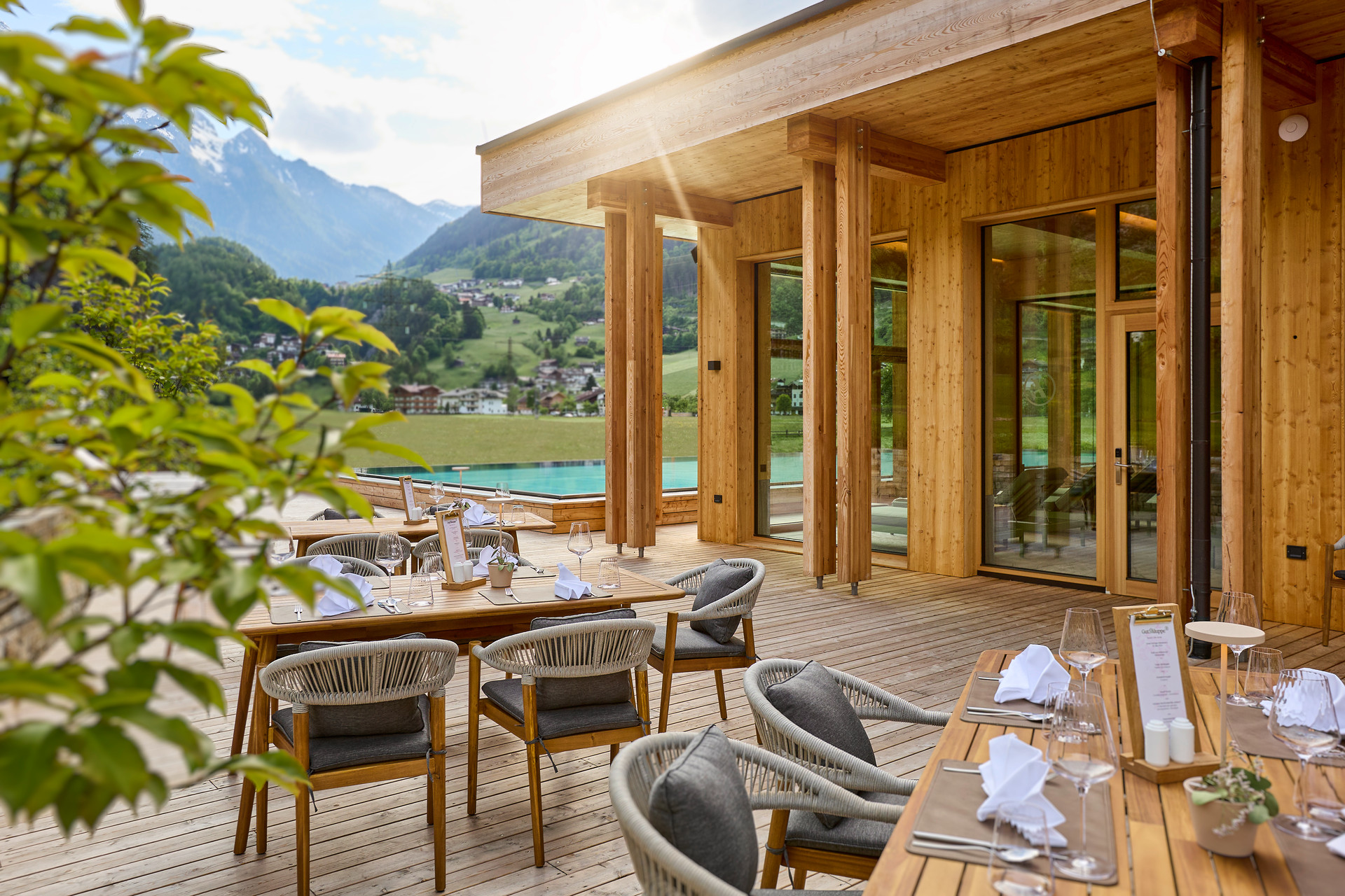 Die Terrasse mit aufgedeckten Holztischen und grauen Stühlen