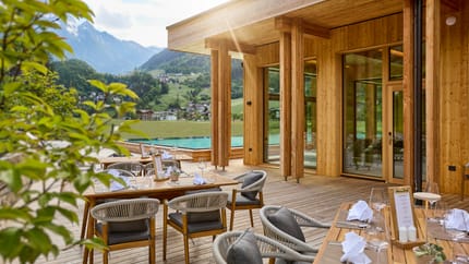Die Terrasse mit aufgedeckten Holztischen und grauen Stühlen