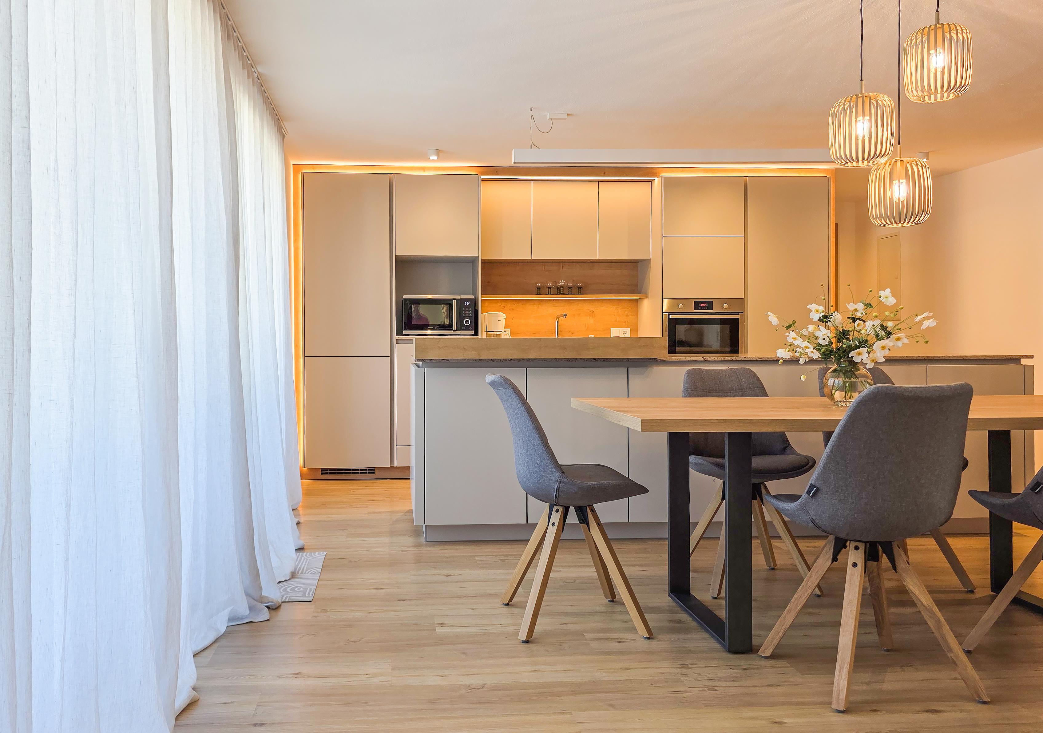 Moderner Küchenbereich mit Esstisch, Stühlen, Hängelampen und Blumenstrauß, helle, freundliche Atmosphäre.