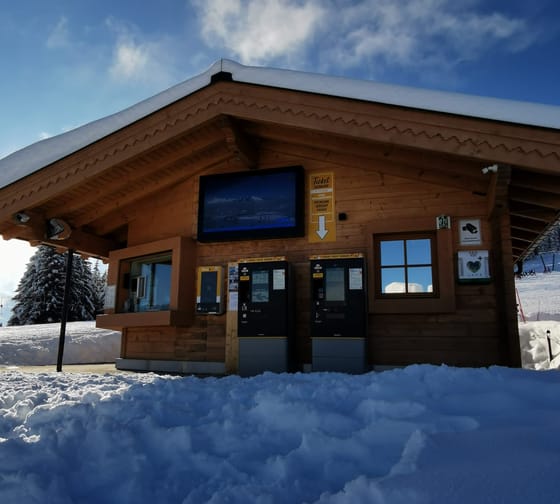 Ein Holzgebäude mit Ticket- und Verkaufsautomaten, umgeben von Schnee, bei klarem Himmel im Winter.