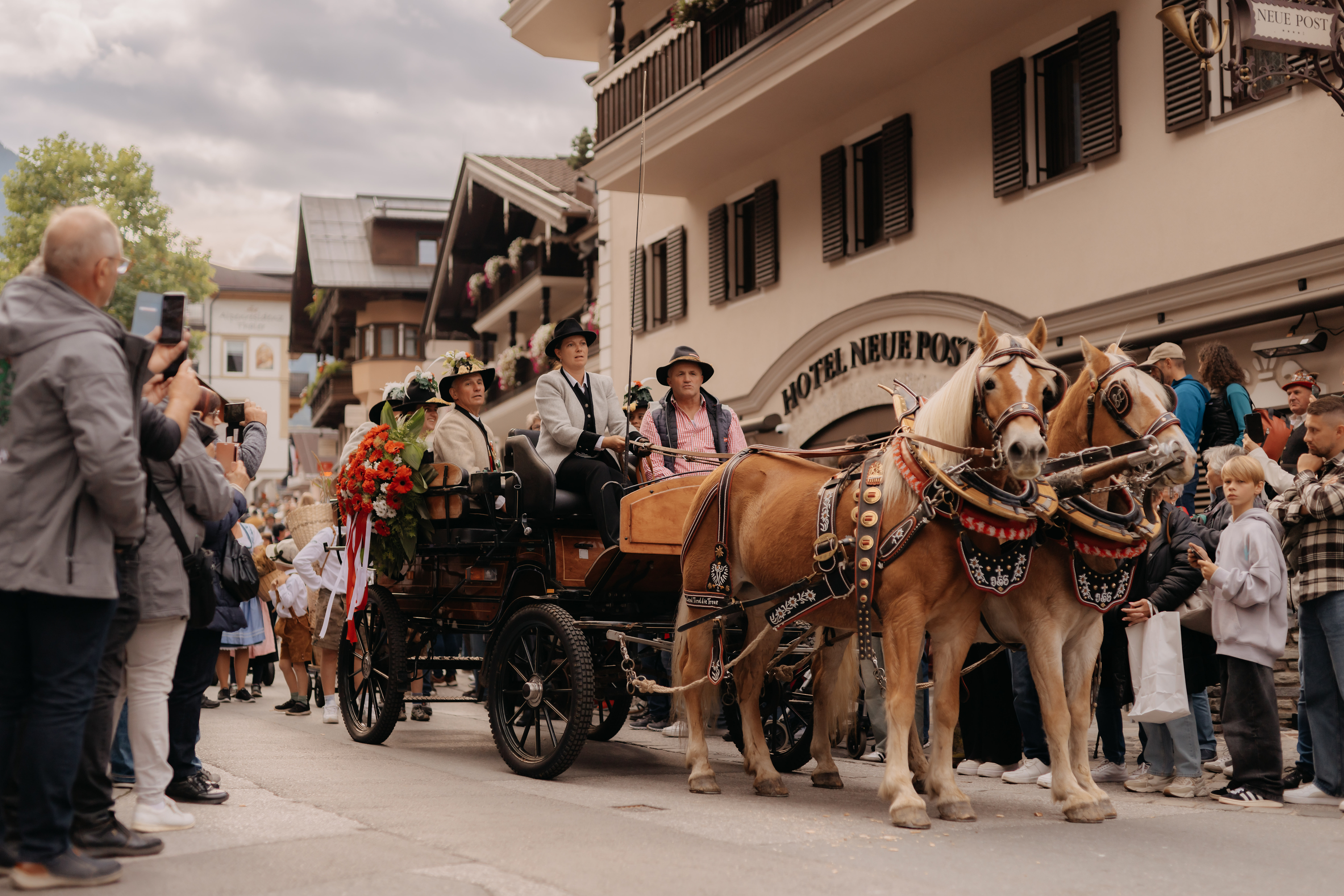 Festively decorated horse-drawn carriage with people wearing traditional costumes at the Zillertal Farmers' and Music Autumn Festival parade in Mayrhofen, accompanied by spectators lining the streets.