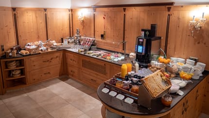 Buffet mit verschiedenen Speisen, Getränken und Geschirr in einer Holz-Küche, warm beleuchtet.