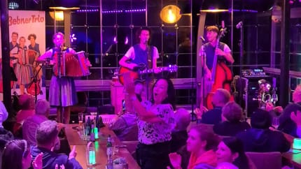 Das Bild zeigt das Mißebner Trio bei ihrem Auftritt und Gästen im Vordergrund.