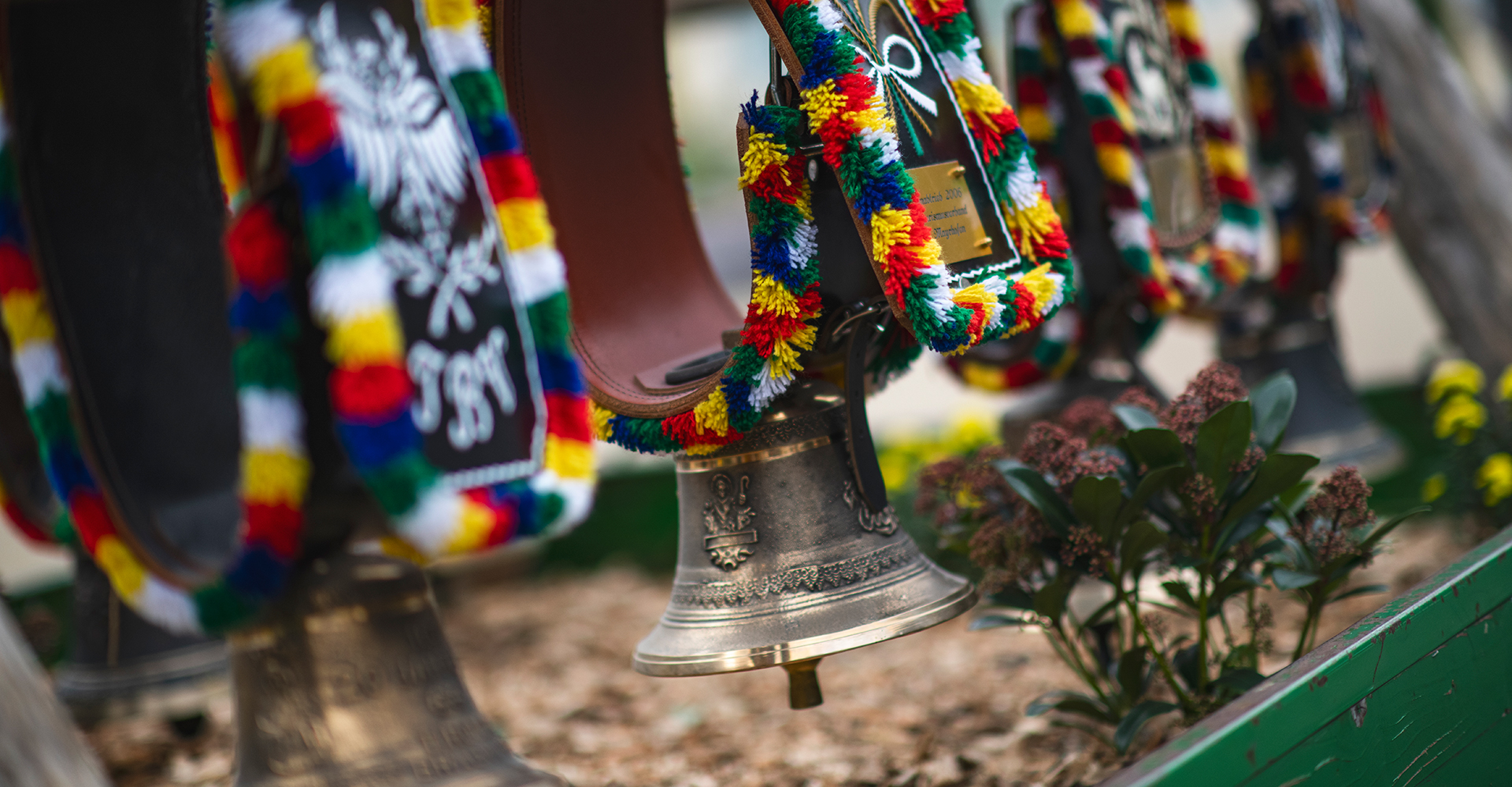 Tractor float during the Zillertal Autumn Festival Parade. A man and two women in Dirndl and Tracht ride a red tractor through a crowded village street, the man lifting his hat. Backed by traditional alpine buildings and a massive snowy mountain.