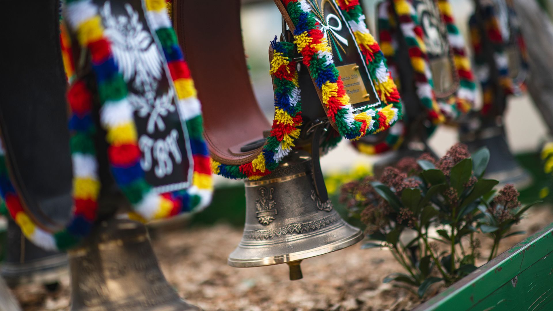 Tractor float during the Zillertal Autumn Festival Parade. A man and two women in Dirndl and Tracht ride a red tractor through a crowded village street, the man lifting his hat. Backed by traditional alpine buildings and a massive snowy mountain.