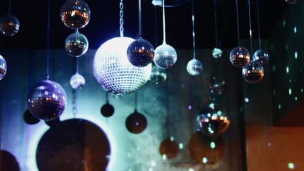 Mehrere kleine Spiegelkugeln hängen an der Decke, Lichtreflexe erzeugen Disco-Atmosphäre, dunkler Raum.