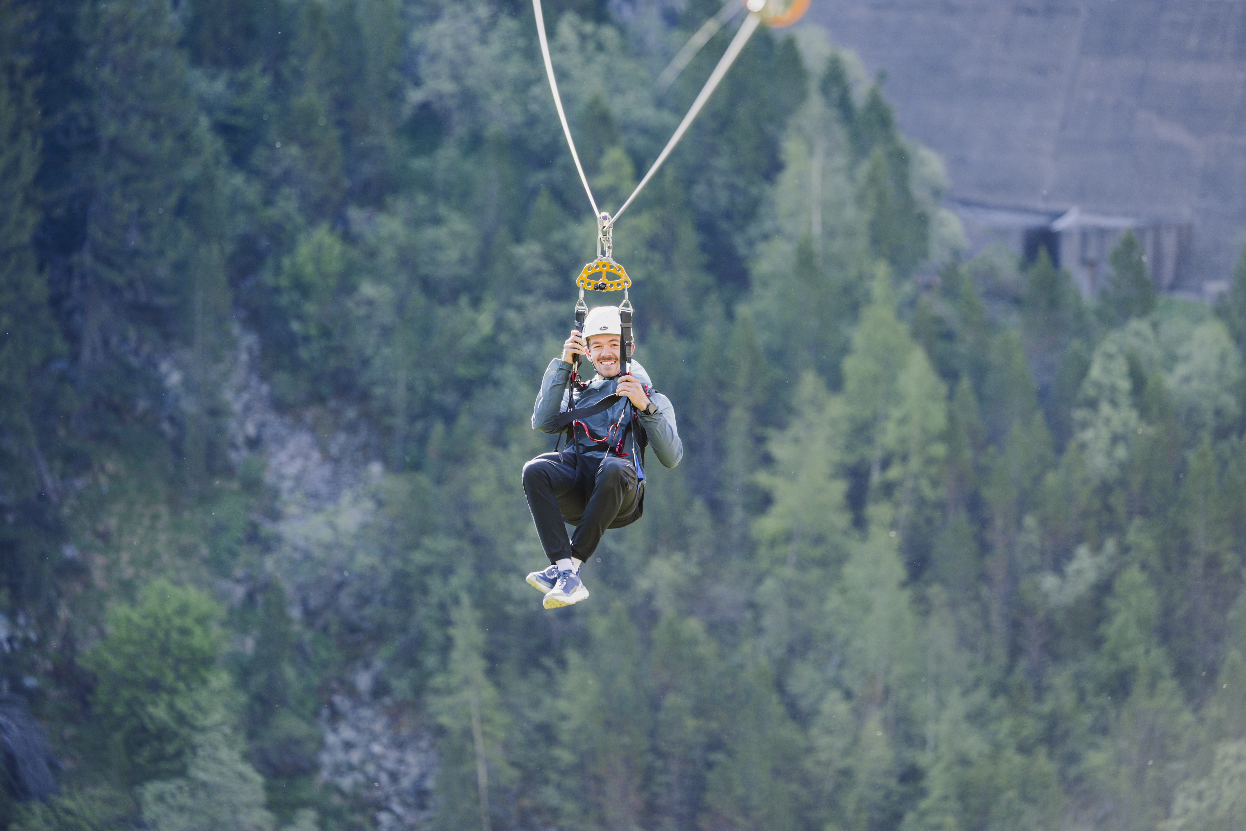 Man ziplining over greenery, wearing a helmet and smiling during the adventure.
