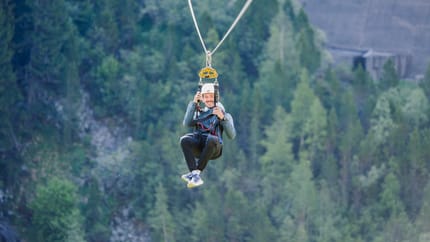 Man ziplining over greenery, wearing a helmet and smiling during the adventure.