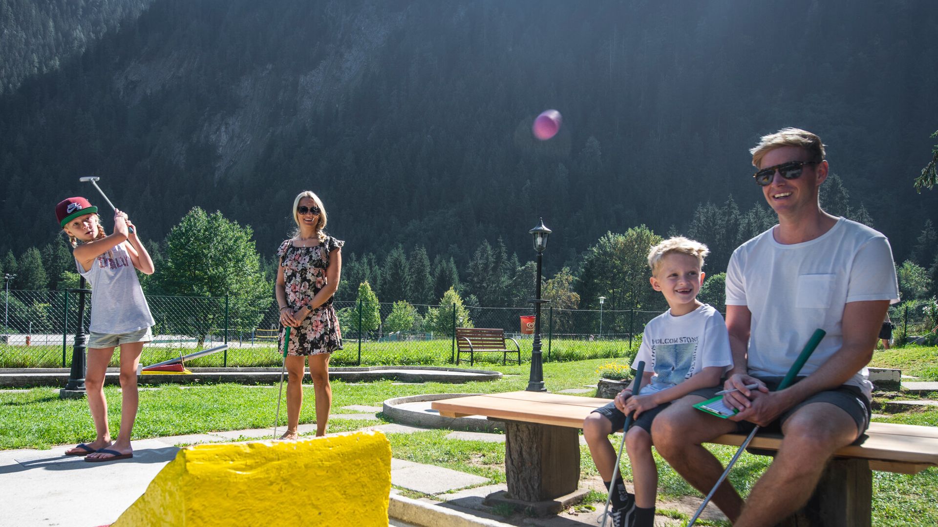 Familienausflug in der Ferienregion Mayrhofen-Hippach im Zillertal, Tirol: Eltern und Kinder spielen gemeinsam Minigolf vor einer beeindruckenden Kulisse aus Bergen und Natur. Sommerliche Freizeitgestaltung für Groß und Klein.