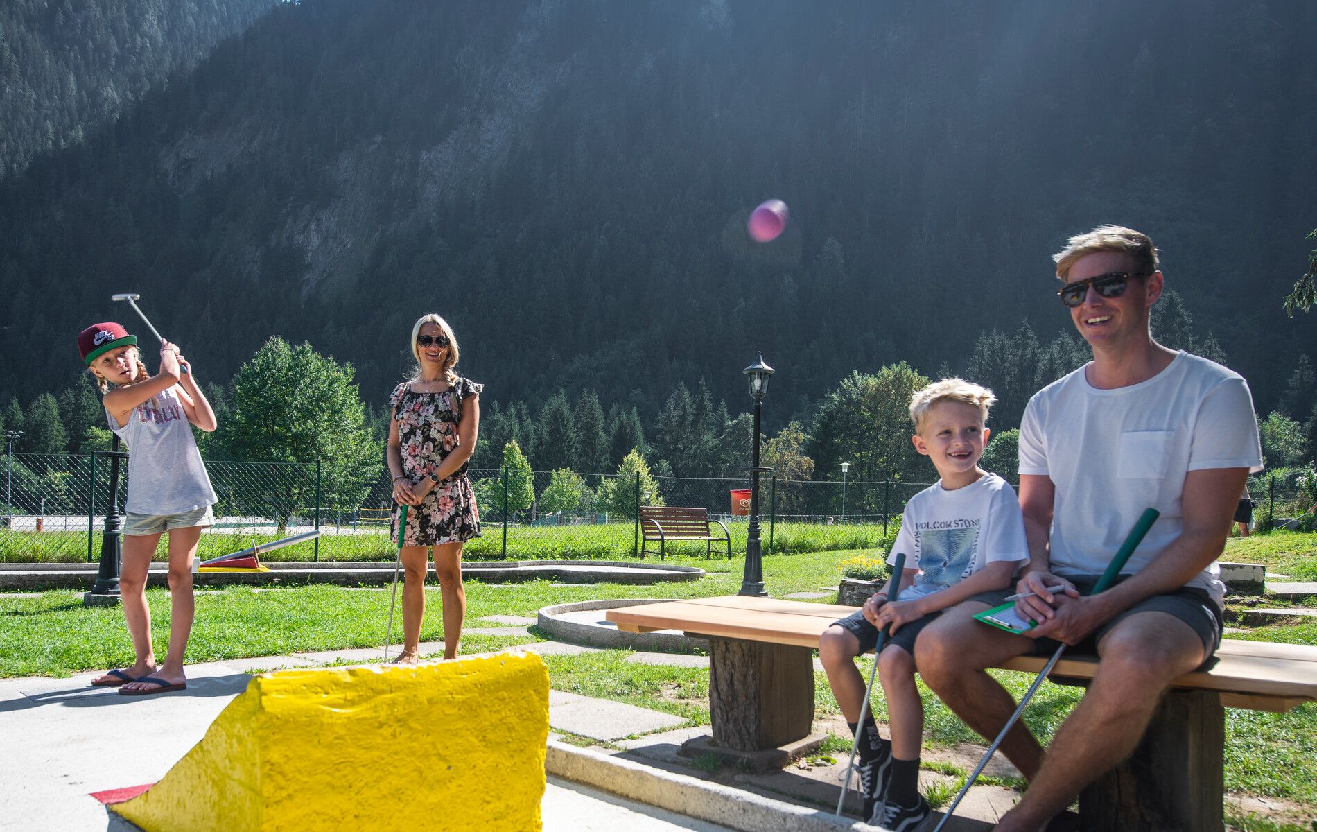 Familienausflug in der Ferienregion Mayrhofen-Hippach im Zillertal, Tirol: Eltern und Kinder spielen gemeinsam Minigolf vor einer beeindruckenden Kulisse aus Bergen und Natur. Sommerliche Freizeitgestaltung für Groß und Klein.