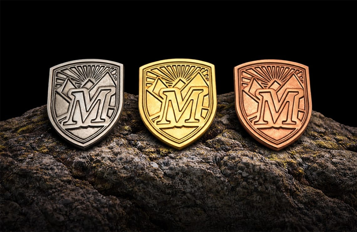 Wanderpass-Abzeichen Mayrhofen-Hippach – Bronze, Silber & Gold Drei Wanderpass-Abzeichen aus Metall in Silber-, Gold- und Bronzefarbe mit stilisiertem Bergmotiv und Schriftzug Mayrhofen-Hippach, auf dunkler Oberfläche nebeneinander arrangiert.