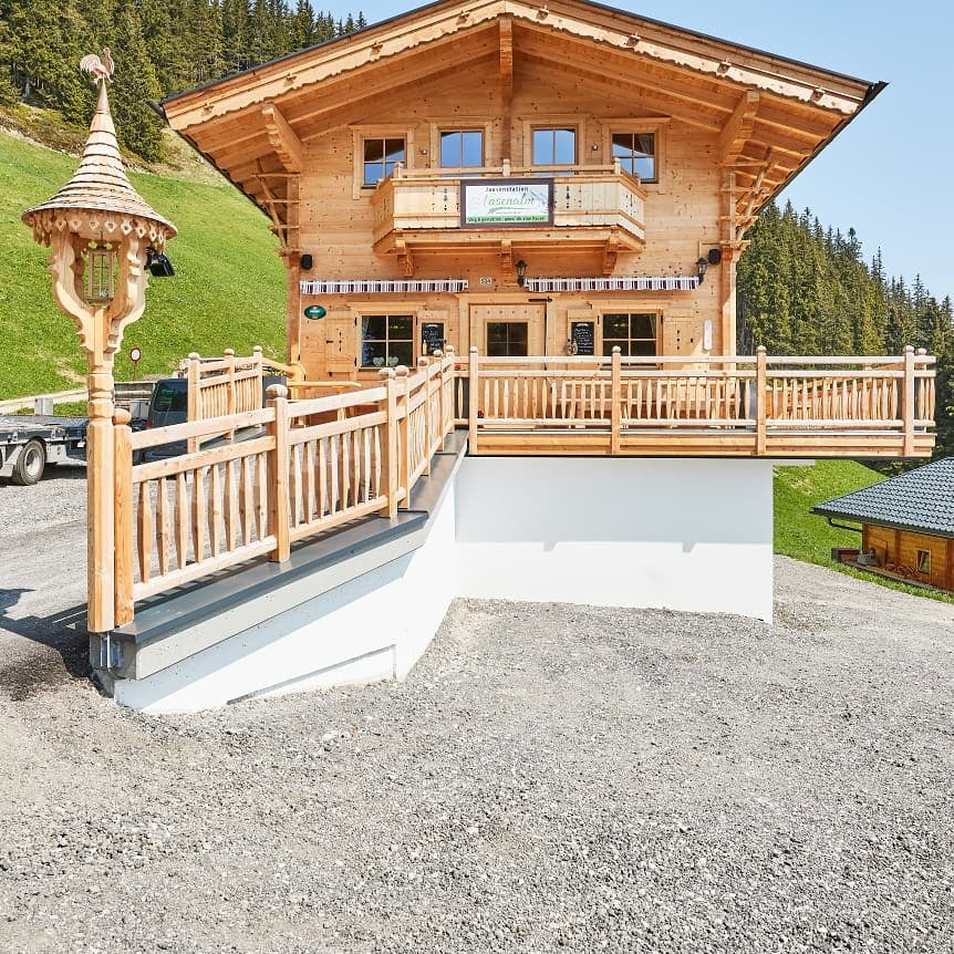 The picture shows the Nasenalm snack station in summer with a meadow and a forest in the background.