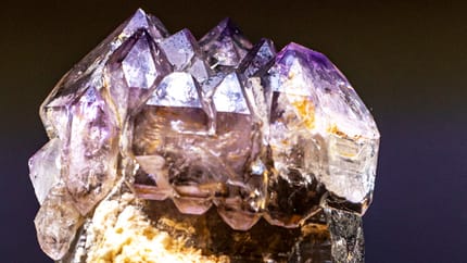 A clear, violet-shimmering crystal with facets and textures, set against a dark background.