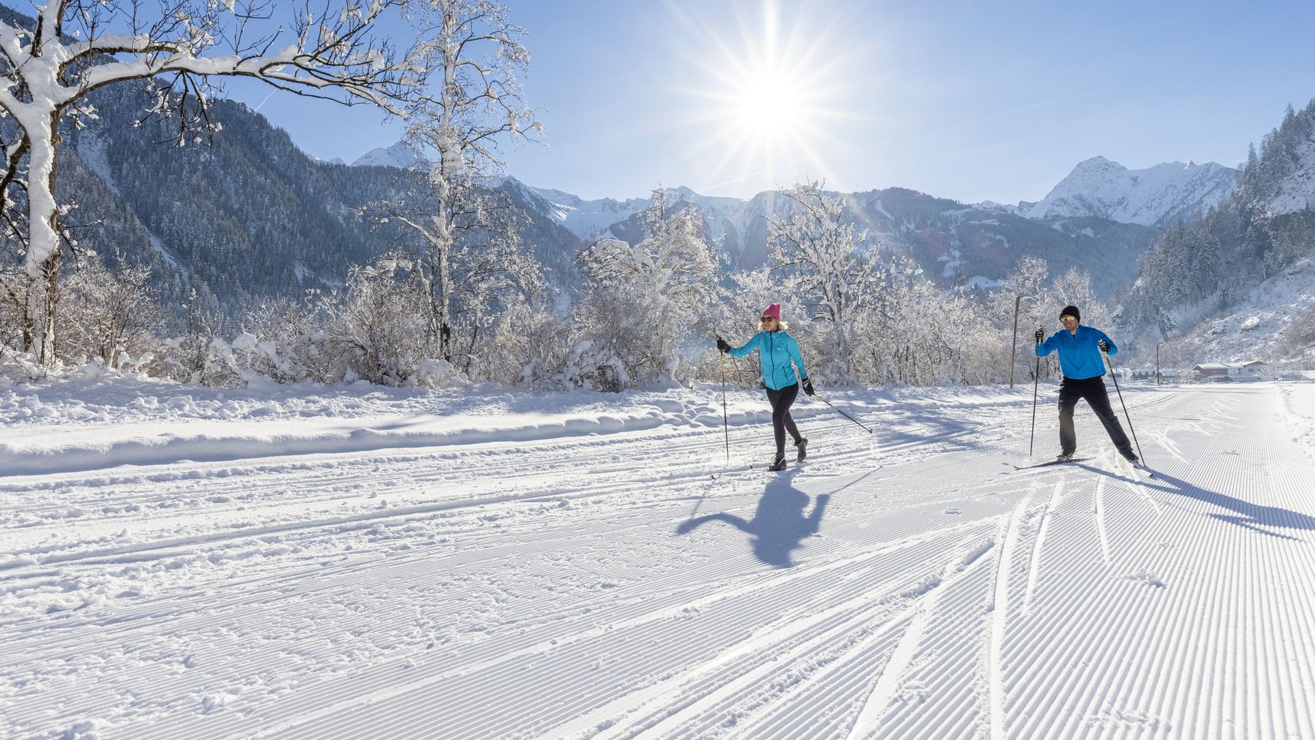 Two cross-country skiers gliding on a freshly groomed trail through a snowy winter landscape with mountains in the background in Mayrhofen-Hippach.
