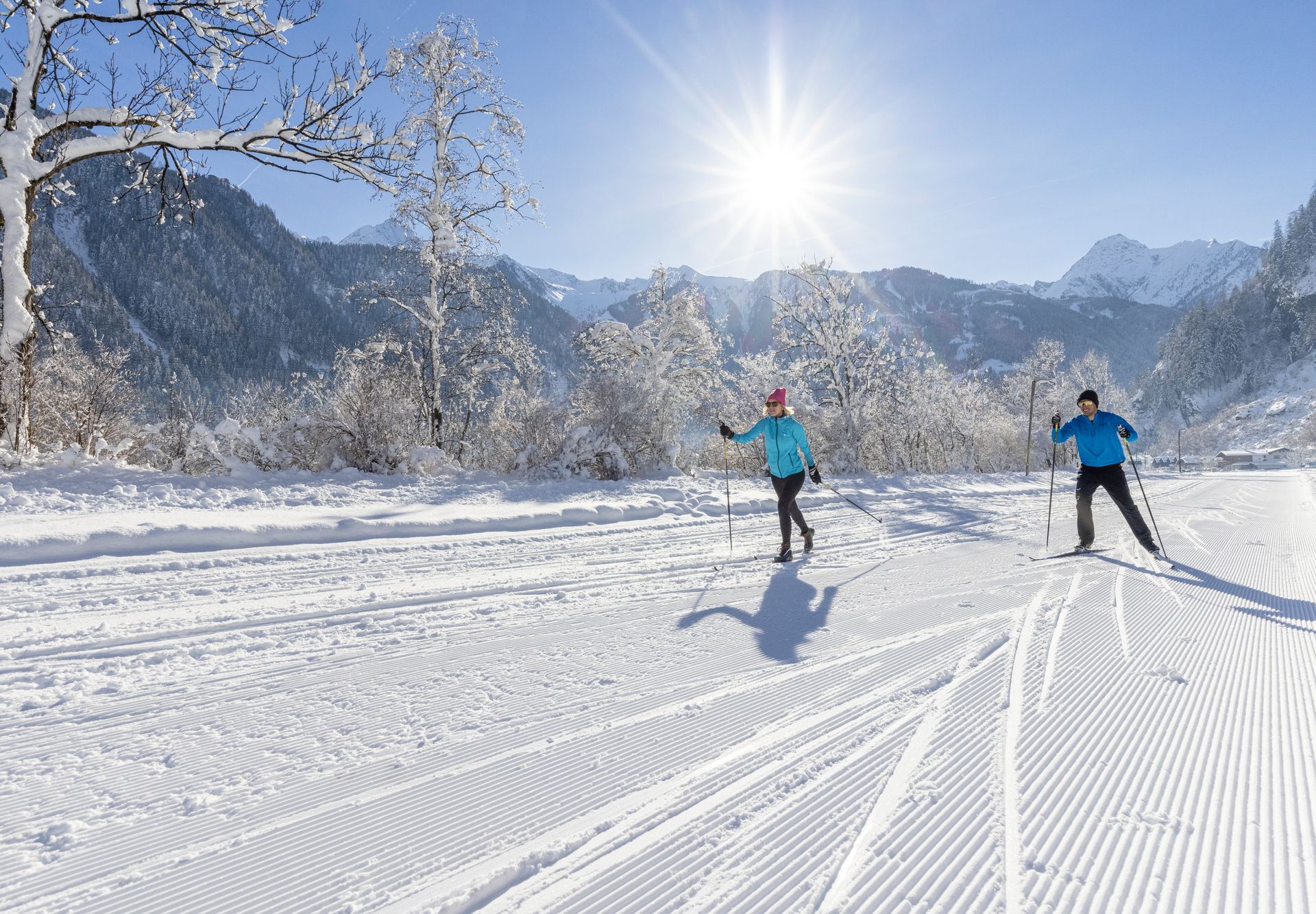 Two cross-country skiers gliding on a freshly groomed trail through a snowy winter landscape with mountains in the background in Mayrhofen-Hippach.