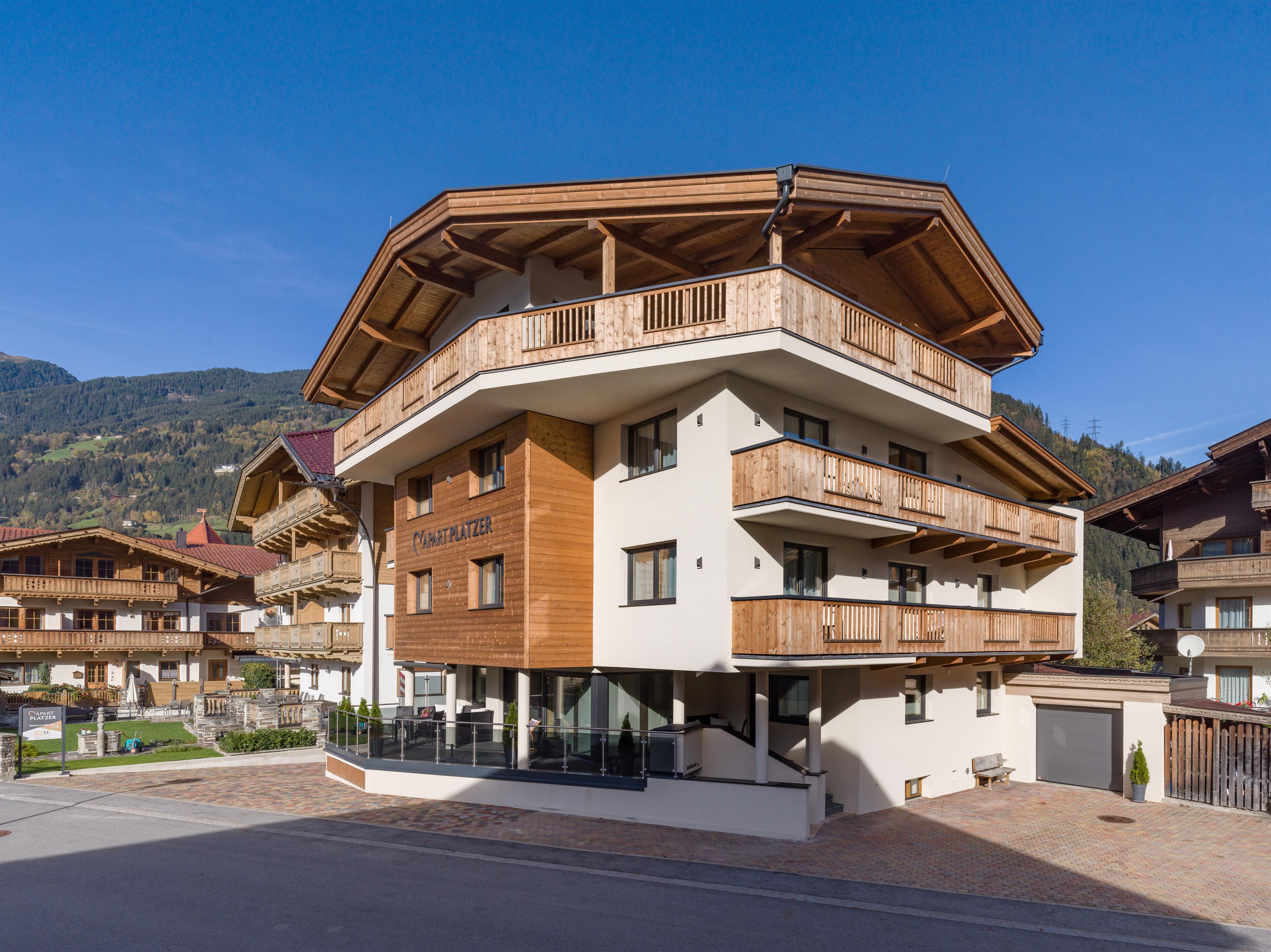 Modernes mehrstöckiges Gebäude mit Holz- und Weißfassade, Balkonen und Bergblick im Hintergrund.