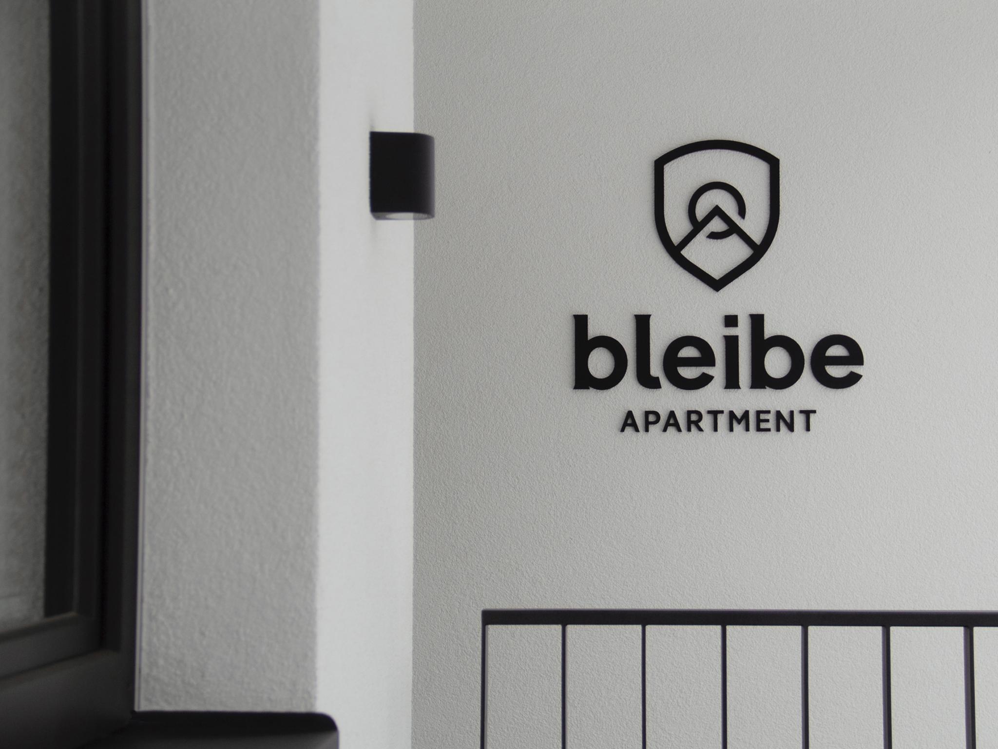 Nahaufnahme eines Schildes mit einem Logo und dem Text 'bleibe APARTMENT' an einer Wand.