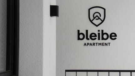 Nahaufnahme eines Schildes mit einem Logo und dem Text 'bleibe APARTMENT' an einer Wand.