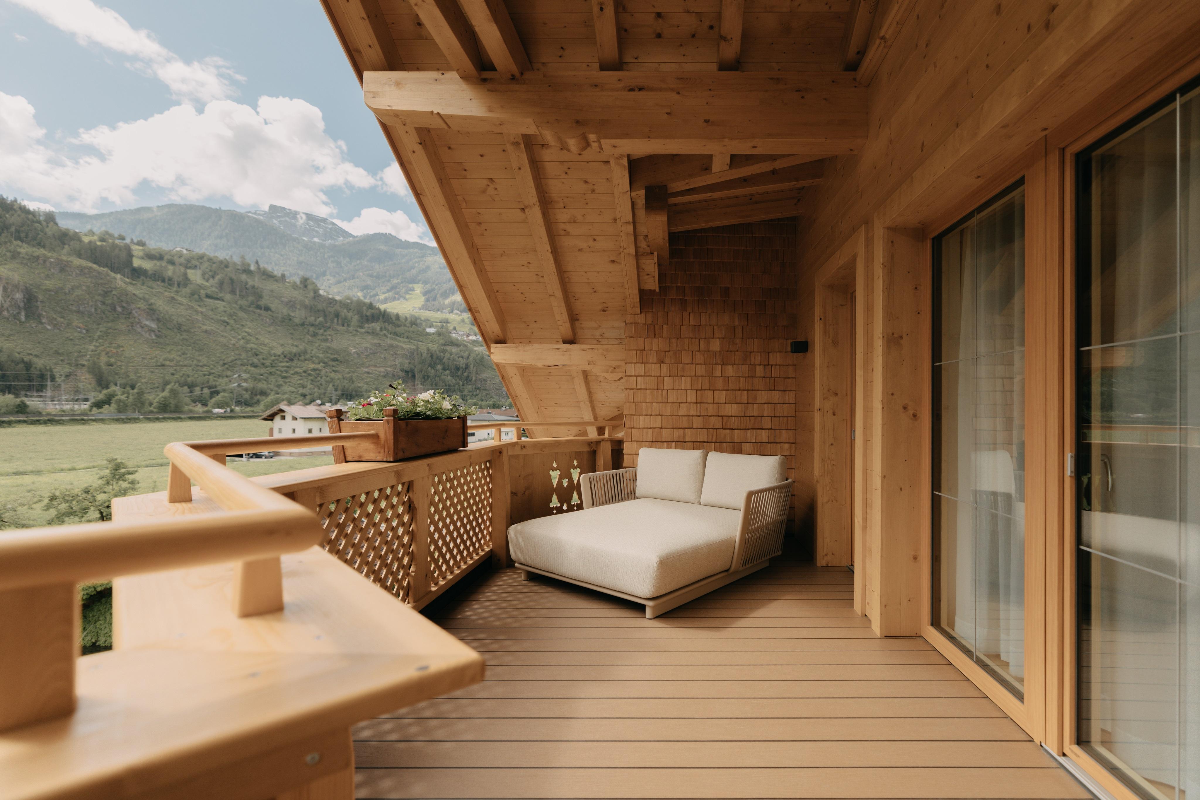 Gemütlicher Balkon mit Holzverkleidung, Sofa und Blick auf Berge und Himmel im Hintergrund.