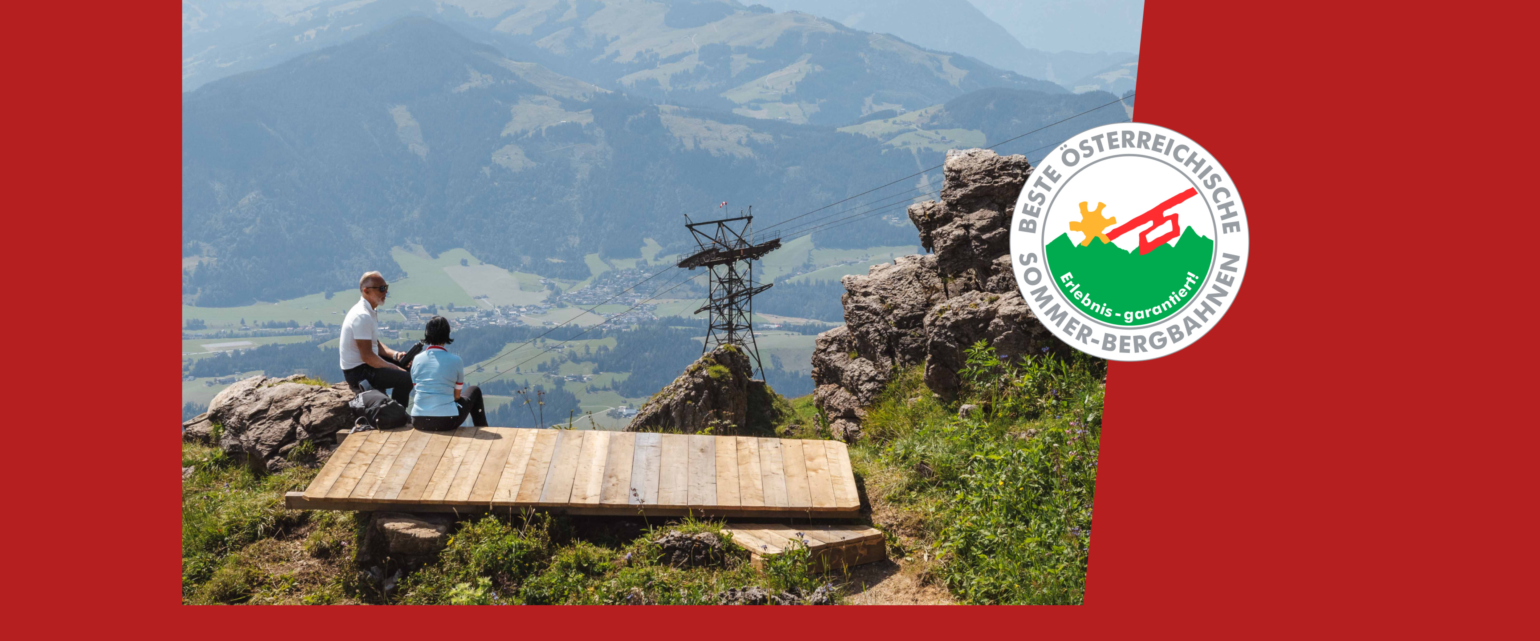 Paar sitzt auf einem Berg mit Panorama und einer Seilbahn im Hintergrund