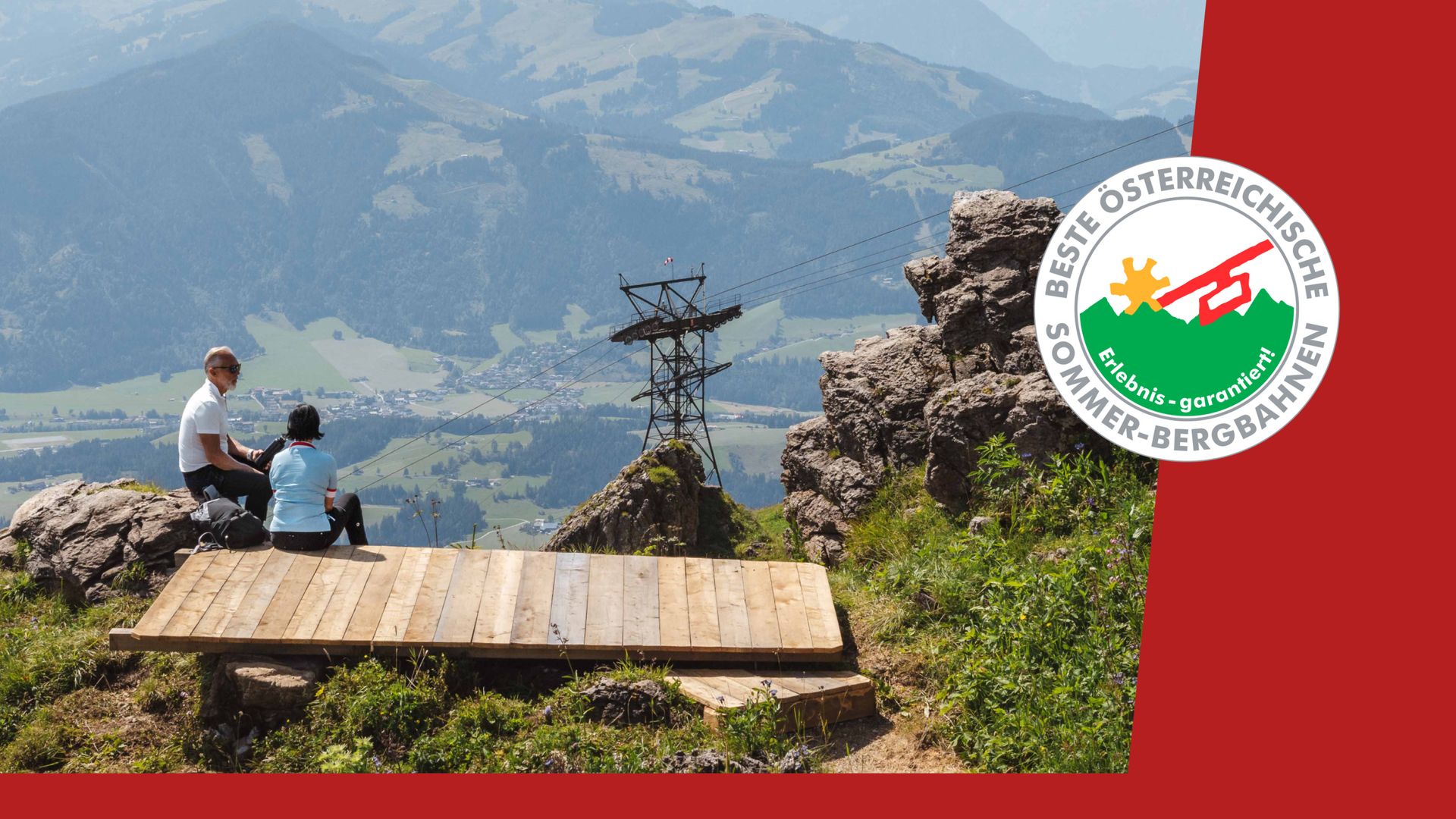 Paar sitzt auf einem Berg mit Panorama und einer Seilbahn im Hintergrund