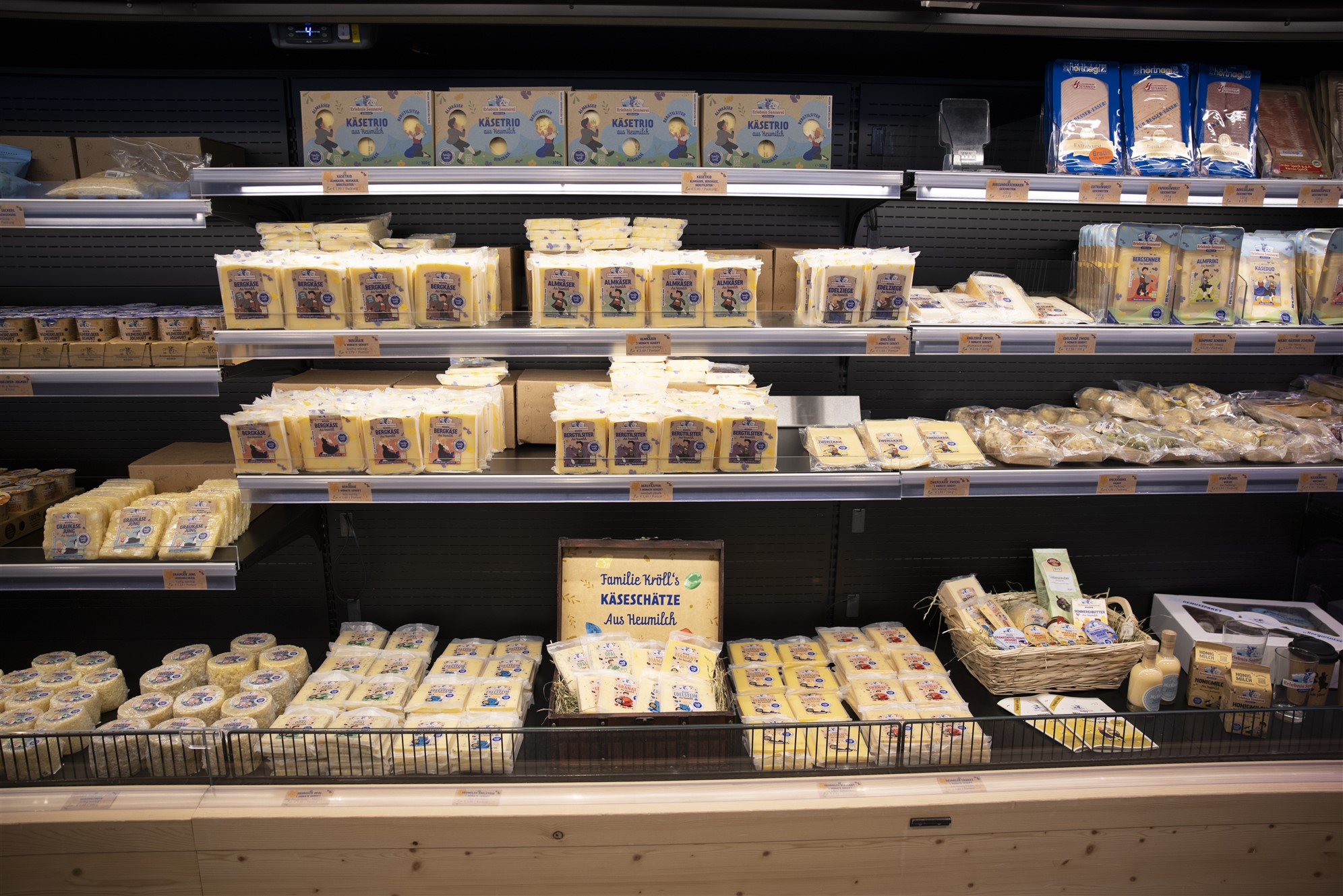 Refrigerated display case with many packaged cheese products. Neatly stacked on several levels, with price tags and labels in the sales area.