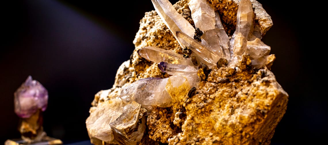 Large, clear crystal on a rock against a dark background, illuminated and shimmering.