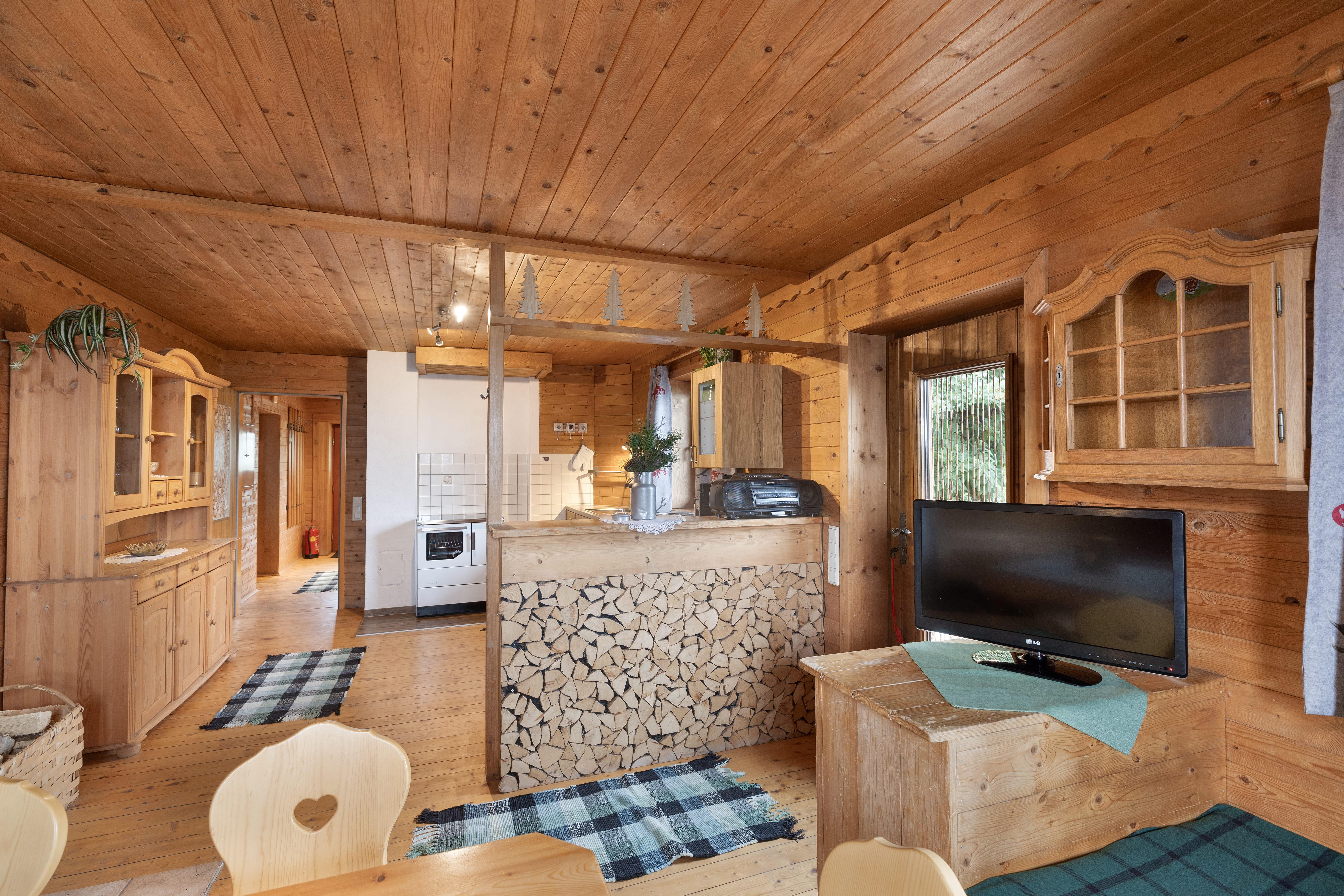 Innenansicht eines Holzhauses mit Küche, Holzdecken, Möbel und Fernseher, gemütlich und rustikal gestaltet.