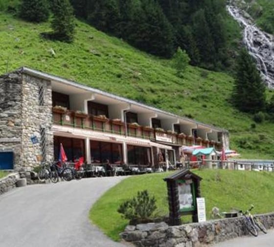 Ein zweistöckiges Hotel an einem grünen Hang mit Fahrrädern und Tischen im Außenbereich, umgeben von Natur und Wasserfall.