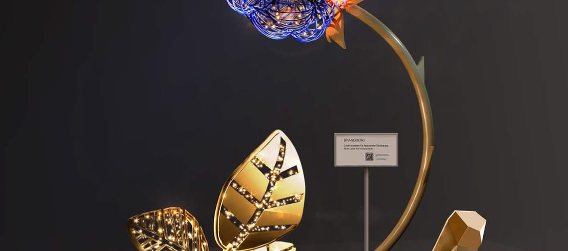 Beleuchtete Kunstinstallation in Brandberg (Tirol): stilisierte Beere mit leuchtenden Punkten auf gebogenem Stiel, davor große goldene Blätter auf einer abstrakten Basis; modernes Lichtobjekt vor dunklem Hintergrund.