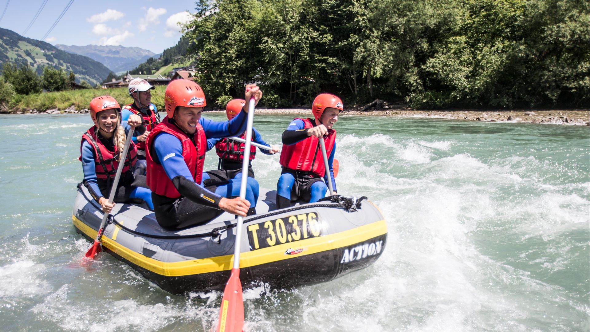 Vier Personen mit Helmen und Schwimmwesten paddeln in einem Schlauchboot den Fluss Ziller in Mayrhofen-Hippach im Zillertal hinunter. Sie genießen die Fahrt durch leichtes Wildwasser, umgeben von grüner Natur und Bergen.