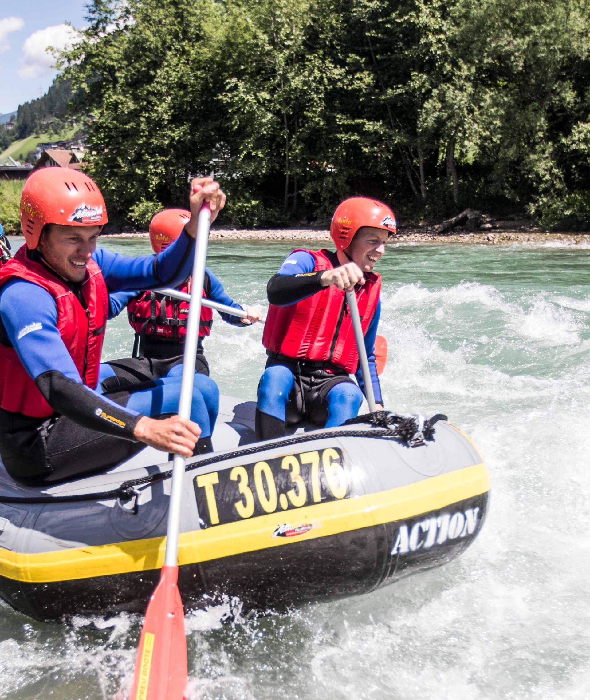 Vier Personen mit Helmen und Schwimmwesten paddeln in einem Schlauchboot den Fluss Ziller in Mayrhofen-Hippach im Zillertal hinunter. Sie genießen die Fahrt durch leichtes Wildwasser, umgeben von grüner Natur und Bergen.