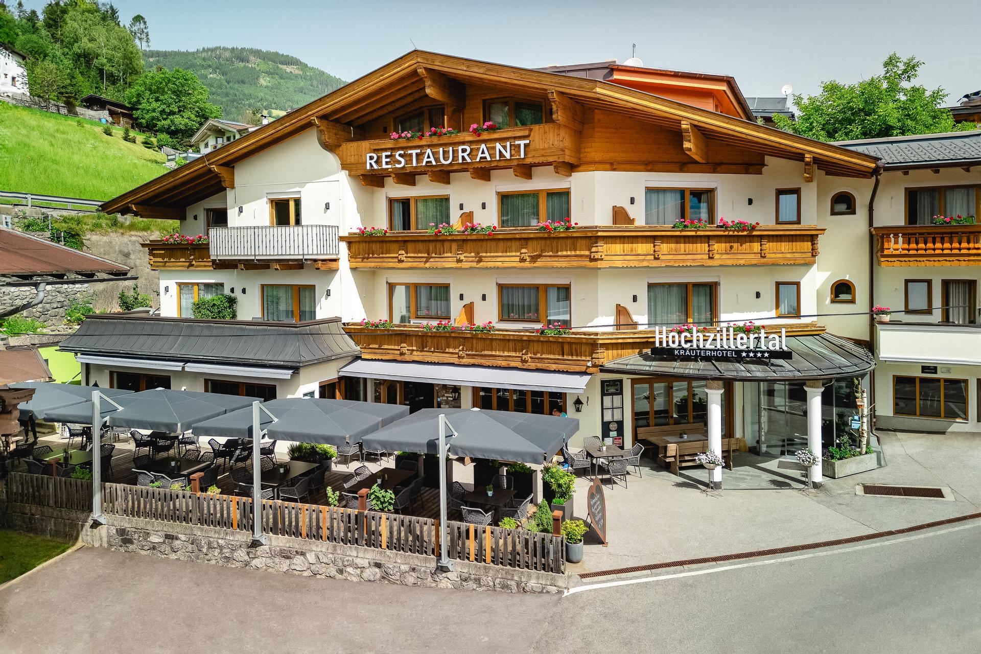 Hotel with a restaurant, wooden balconies, flowers, and an outdoor seating area with tables and umbrellas.