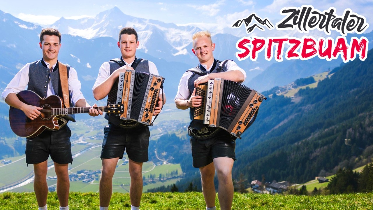 Drei junge Männer mit traditionellen Trachten, spielen Gitarre und Akkordeon vor Bergkulisse, Titel: Zillertaler Spitzbuam