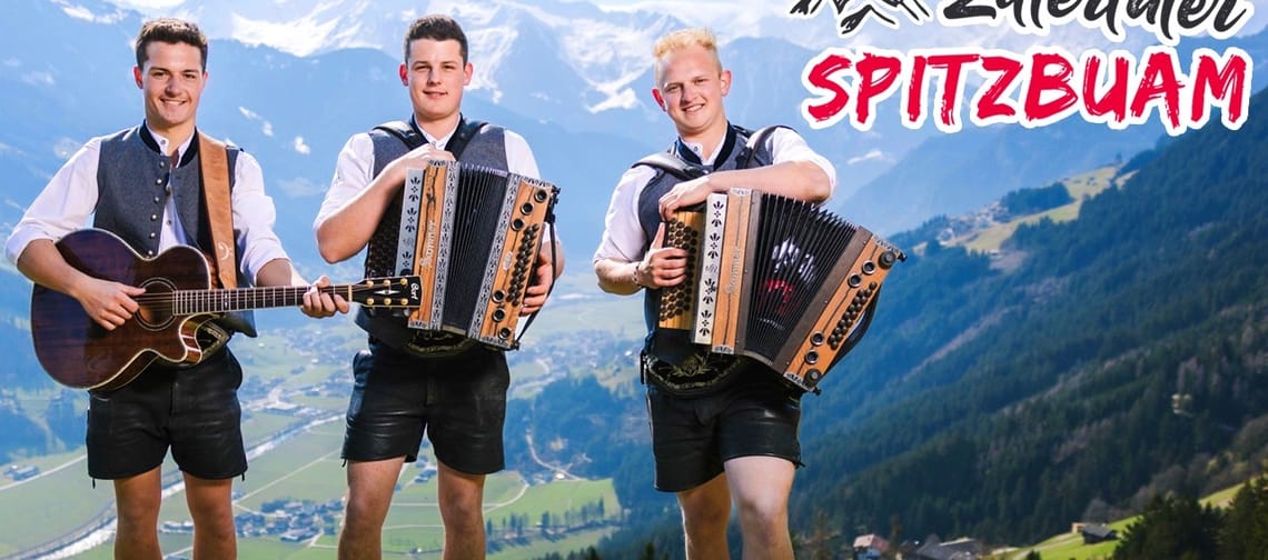 Drei junge Männer mit traditionellen Trachten, spielen Gitarre und Akkordeon vor Bergkulisse, Titel: Zillertaler Spitzbuam