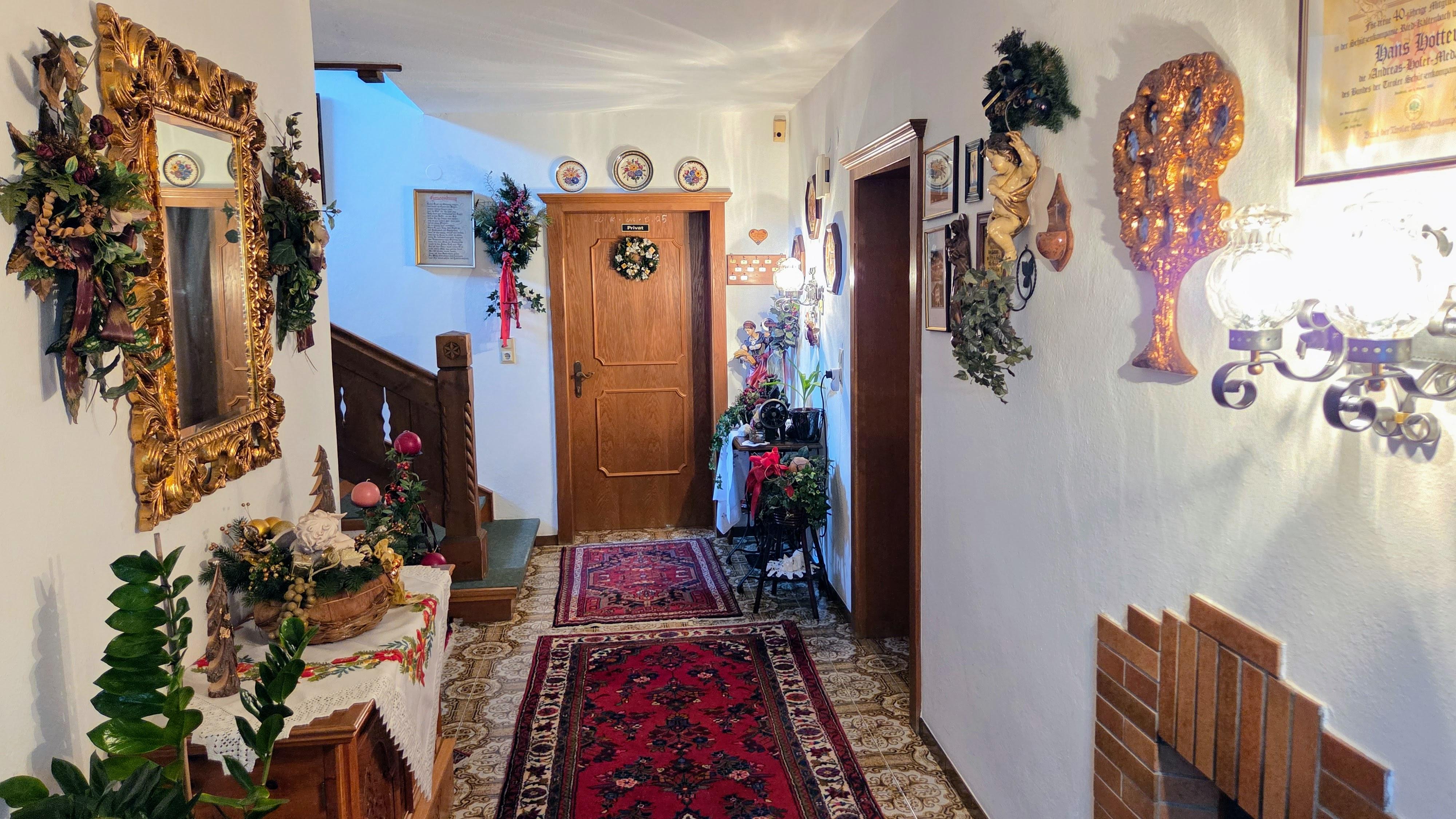 Ein festlich dekorierter Flur mit Spiegel, Pflanzen, Wandbildern und einem roten Teppich im Eingangsbereich.