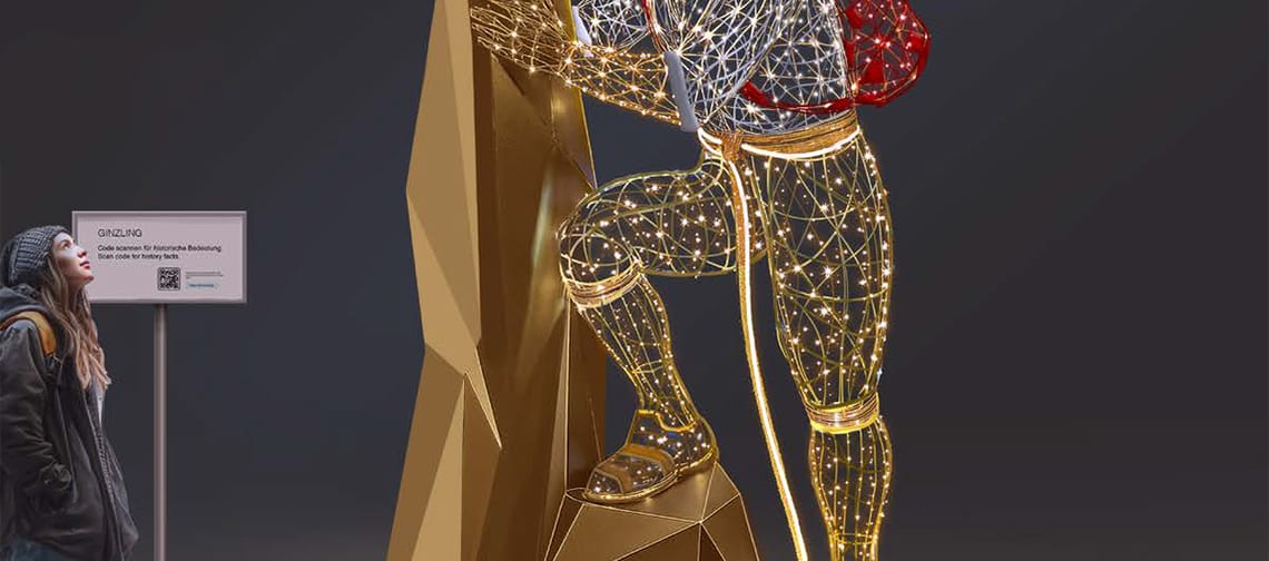 Beleuchtete Skulptur eines Bergsteigers in Ginzling (Tirol): stilisierte Figur aus goldenen Lichtlinien mit rotem Rucksack lehnt an einer geometrischen Felsform; links eine Person betrachtet die Installation vor dunklem Himmel.
