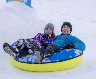 Adult and child laughing while snowtubing at Winterzauber Ginzling in the Zillertal Valley