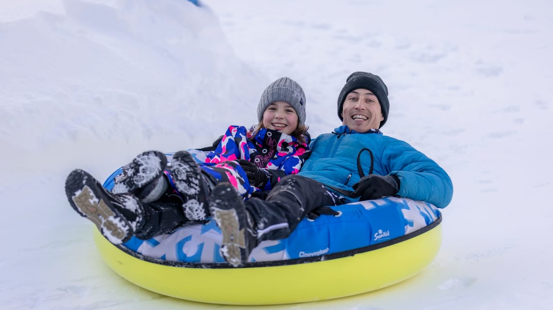 Erwachsener und Kind lachen beim Snowtubing im Winterzauber Ginzling im Zillertal