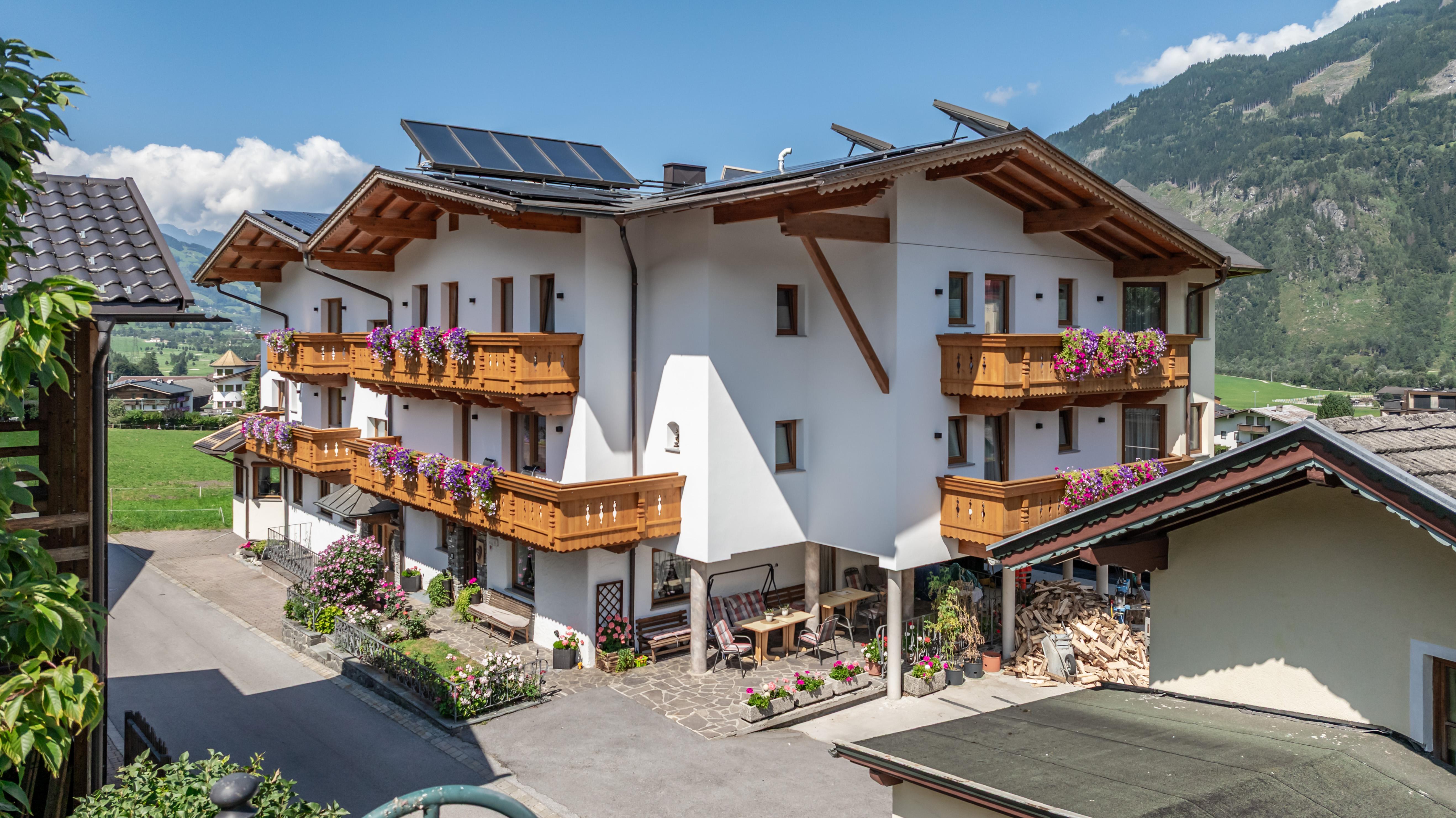 Multi-story house with wooden balconies, blooming flowers, and mountains in the background.