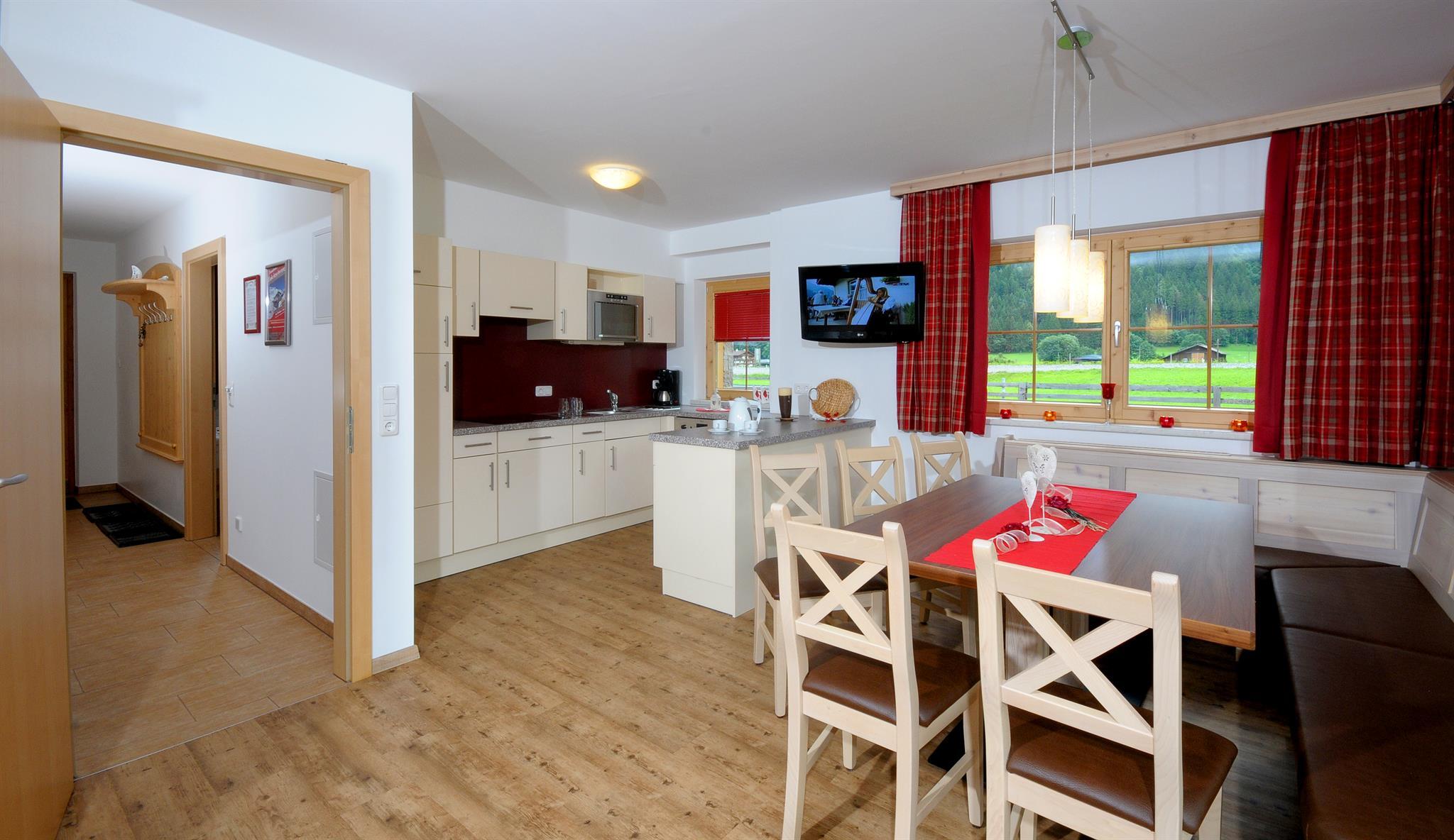 Bright kitchen and dining area with large windows, red curtains, wooden furniture, view of greenery outside.