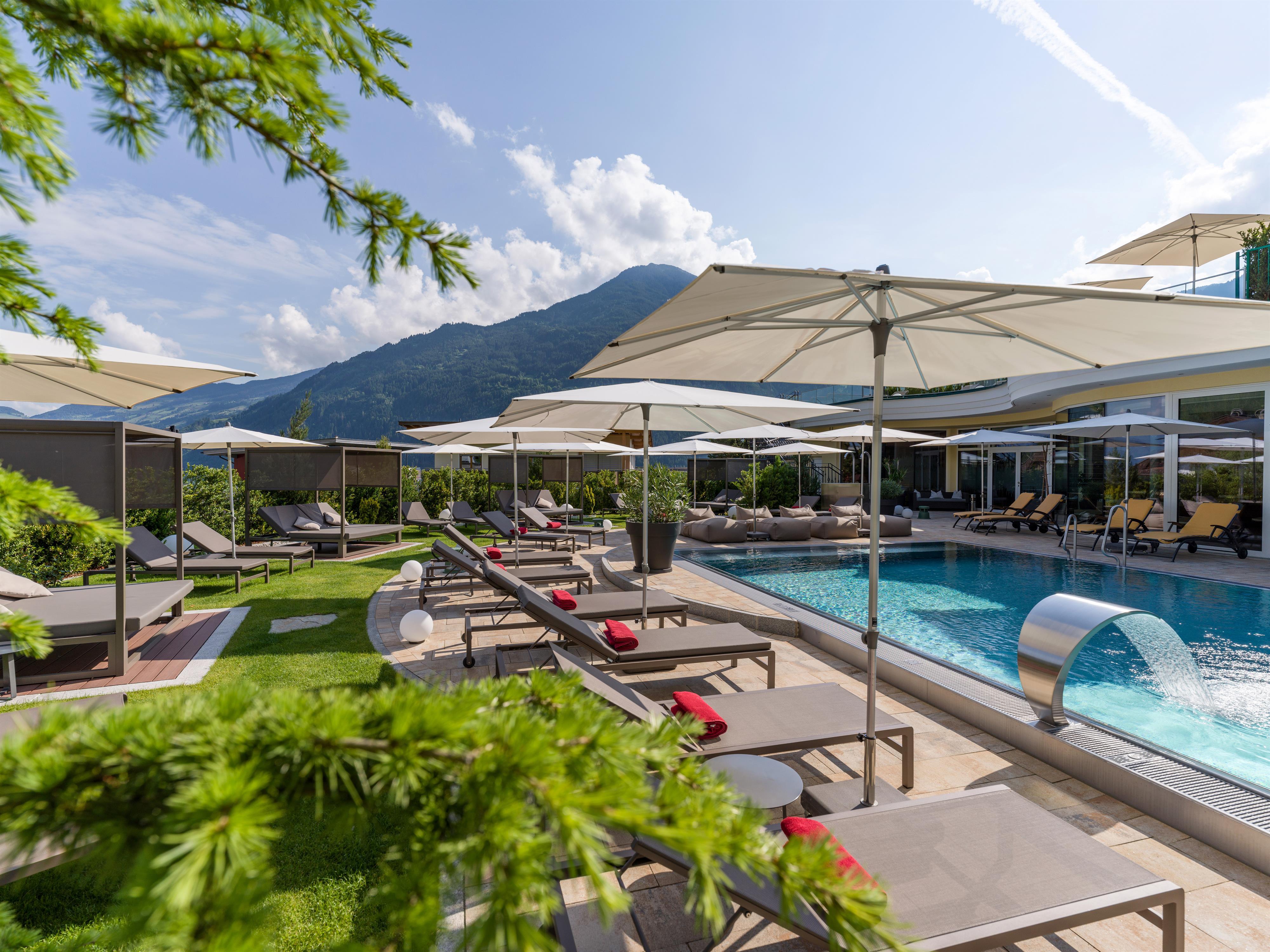 Poolbereich mit Liegen, Sonnenschirmen und Bergblick bei schönem Wetter.