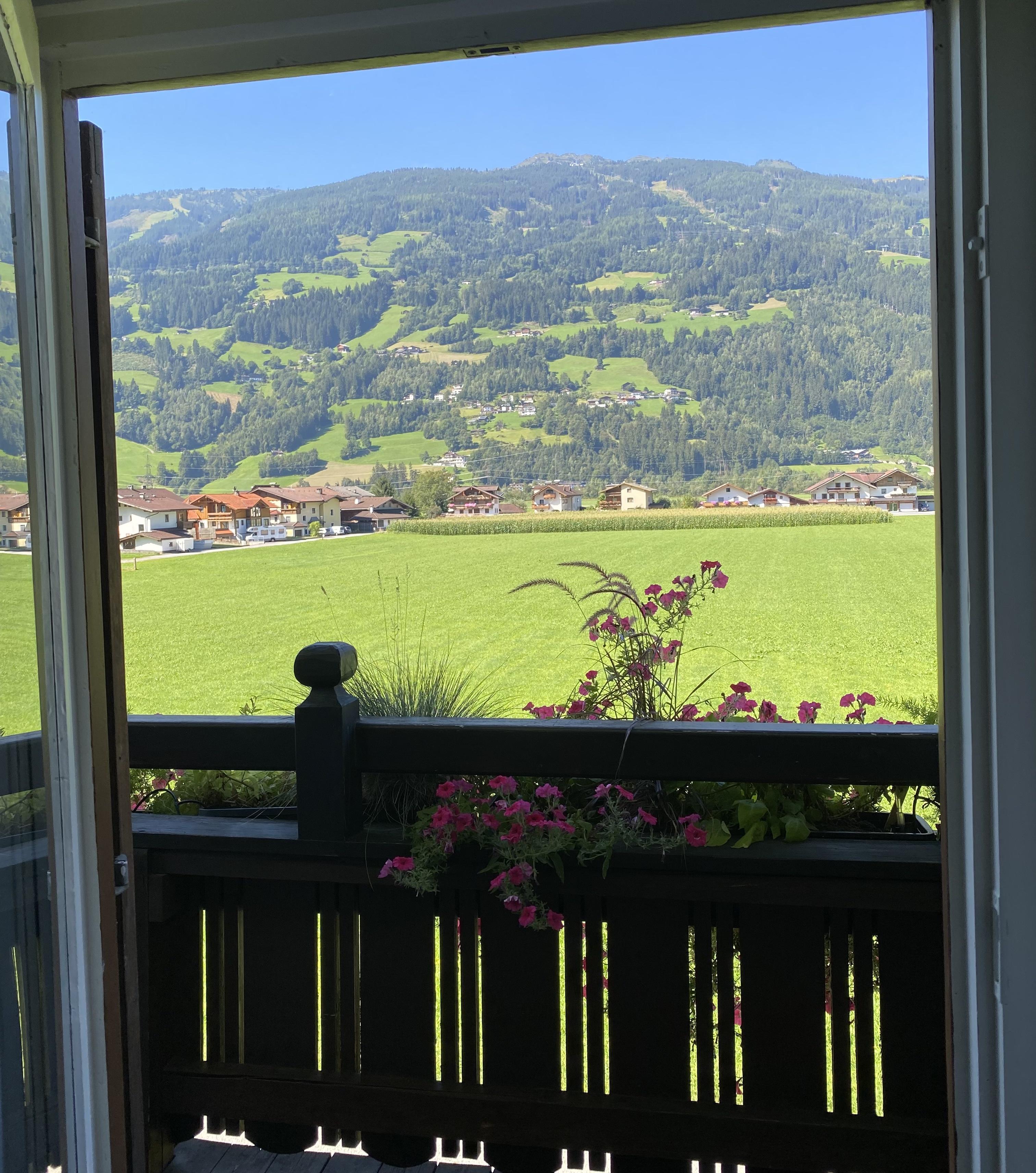 Blick aus einem Fenster auf grüne Hügel und Häuser in einer ländlichen Gegend bei schönem Wetter.