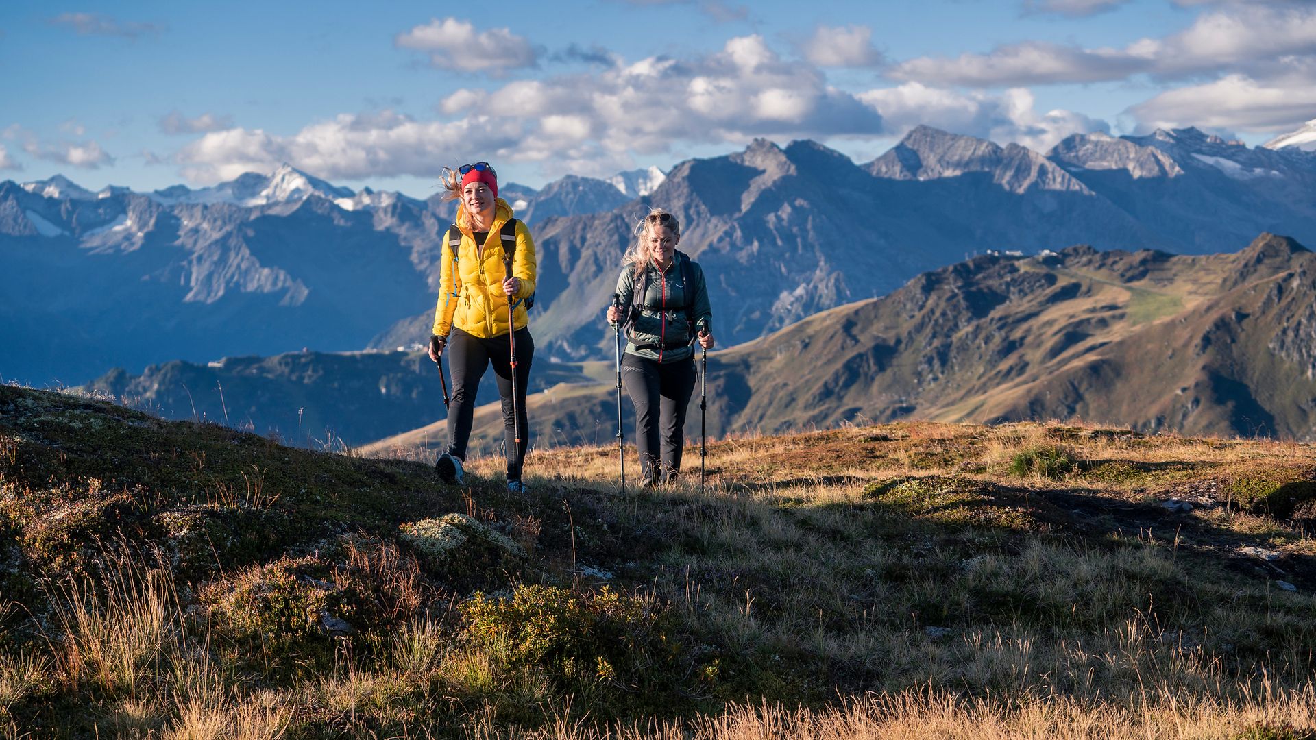 Zwei Wanderinnen mit Stöcken in den Alpen oberhalb von Mayrhofen-Hippach, sonniger Tag mit klarer Sicht auf Berggipfel – sicheres Wandern in eindrucksvoller Tiroler Berglandschaft.