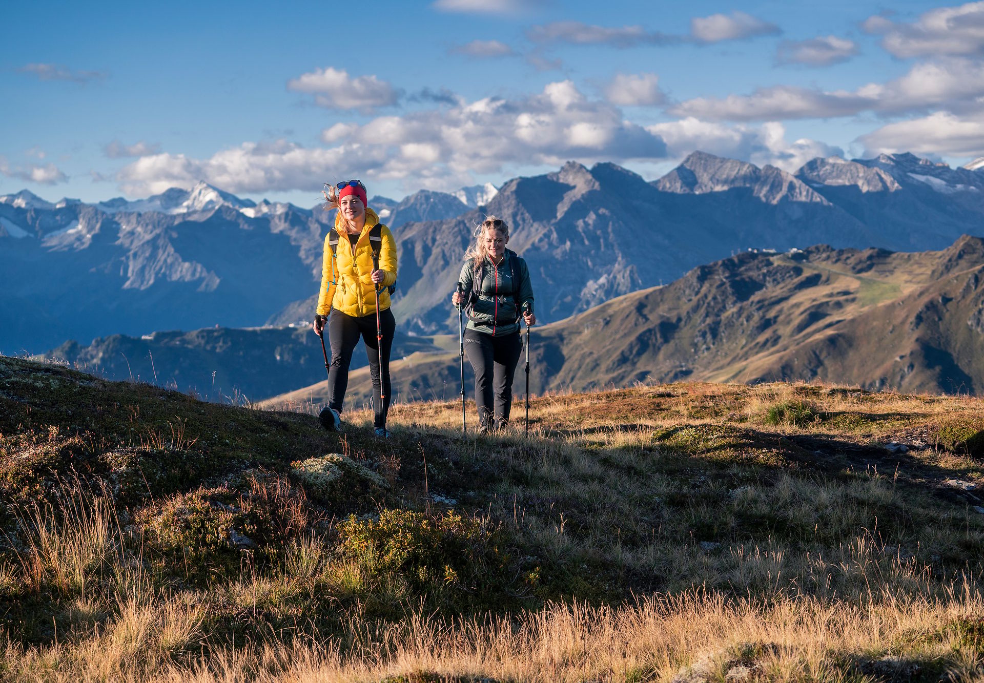 Zwei Wanderinnen mit Stöcken in den Alpen oberhalb von Mayrhofen-Hippach, sonniger Tag mit klarer Sicht auf Berggipfel – sicheres Wandern in eindrucksvoller Tiroler Berglandschaft.